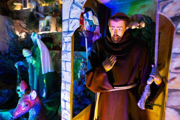 Fototapeta premium Christmas nativity crib scene in church. Franciscan monk doll with bell.