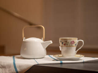 CUP OF TEA AND WHITE TEAPOT IN WARM KITCHEN. HOMELIKE. RELAXING MOMENT. SELECTIVE FOCUS
