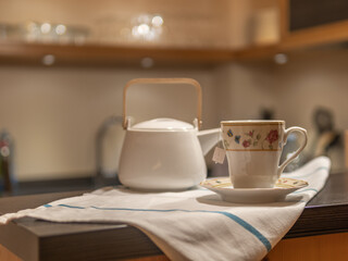 CUP OF TEA AND WHITE TEAPOT IN WARM KITCHEN. HOMELIKE. RELAXING MOMENT. SELECTIVE FOCUS