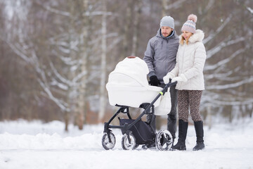 Young family pushing baby stroller and walking on snow covered sidewalk at park in cold winter day....