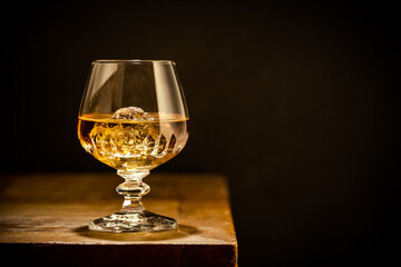 Whiskey with ice or brandy in glass on rustic wooden table over black background with copy space
