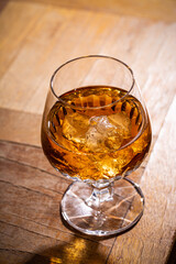 Whiskey with ice or brandy in glass on rustic wooden background with copy space