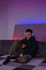 Fototapeta na wymiar Teenage boy using phone in his room with neon light.
