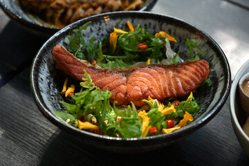 Close up view of fried salmon steak with edible wild flowers and vegetables on wooden table