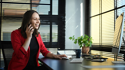 Attractive caucasian businesswoman having cell phone conversation and working on computer at modern office