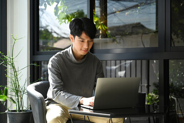 Handsome asian man freelancer using laptop and working on online project remotely in outdoor cafe