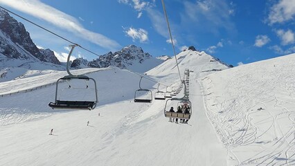 Chimbulak ski resort  near the city of Almaty, Кazakstan 01.07.2023.
Ski lift in winter mountain landscape. View over a ski resort with people in chair lifts and majestic mountains in the background