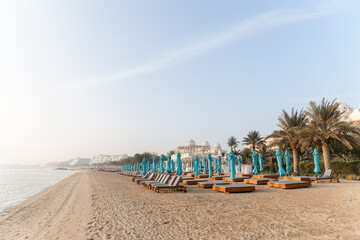 Beautiful empty beach with umbrellas and wooden sun loungers. A perfect place for a summer vacation. Dawn on an empty beach with the sea and buildings as a backdrop. 