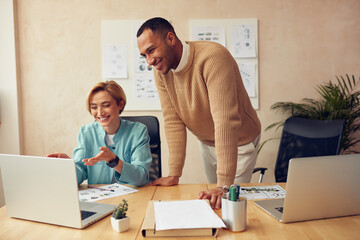 Cheerful Businesspeople Working Computer At Office. Happy Colleagues Couple Discussing Laptop Screen In Modern Office. Teamwork Concept