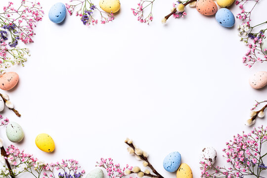 Beautiful Easter composition with spring flowers and colorful quail eggs over white background. Springtime and Easter holiday concept with copy space. Top view