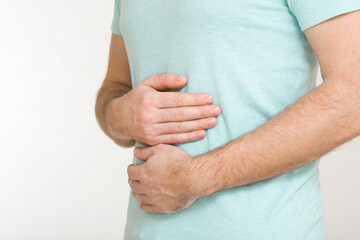 Young adult man touching painful belly with arms isolated on light gray background. Closeup. Side view. Suffering from stomach ache.