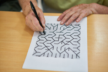 Hand von Seniorin mit Stift beim Labyrinth Rätsel lösen
