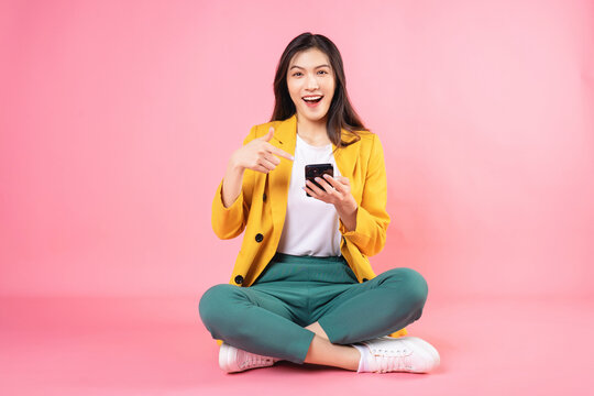 Image of young Asian businesswoman sitting and holding smartphone on background