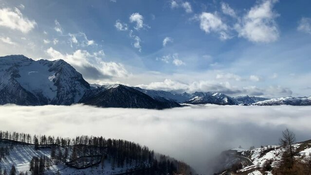A white and soft cloud fill completely the valley in a winter day. All around there are snow capped mountain lighted from a warm morning sun. pan camera movement