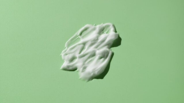 Macro crane shot of white cosmetic lotion smears on green background | White cosmetic lotion commercial