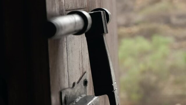 Plano detalle de pestillo antiguo abriendo una puerta de madera antigua con mano 