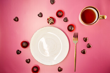 Obraz na płótnie Canvas White mock up vintage plate with fork and cup of tea on pink gradient background. Chocolate hearts and decorated sweets. Romantic dinner, Valentines Day concept. View from above