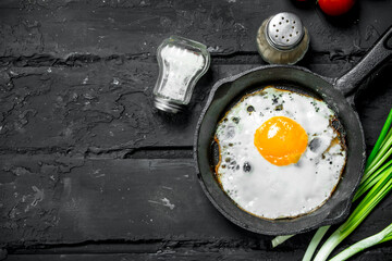 Fried eggs in a pan with green onions and tomatoes.