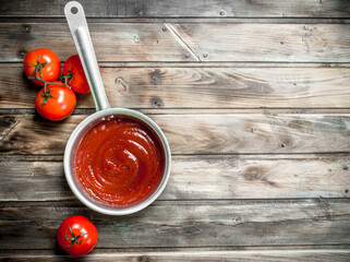 Tomato sauce in a saucepan and ripe tomatoes.