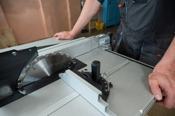 Close-up of a man cutting a wooden board on a circular machine.