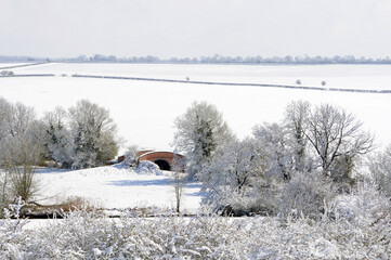 A bridge over the Oxford Canal covered in snow with fields and sunshine