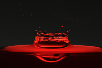 A drop of red water forming a coronet as it splashes into a glass full of liquid, backlit for contrast.