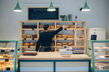 Rear view of man arranging bread on shelf in bakery