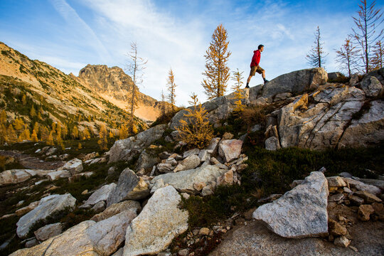 A young man walks on a rock beneath steep mountains of the Cascades in the Pasayten Wilderness on the Pacific Crest Trail (PCT) in Washington.