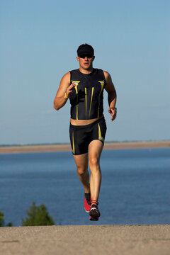 A male athelete running while training for a triathlon at a lake.