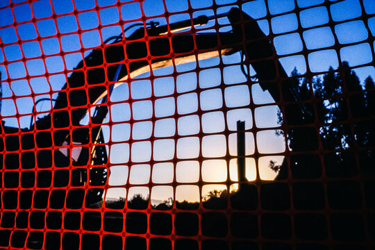 Backhoe at construction site seen through temporary red fencing at sunset