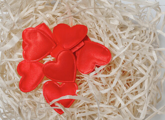 Many red hearts on decorative wooden shavings. Decoration of gifts.