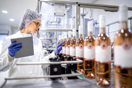 Female factory expert controlling wine production in alcohol beverage bottling plant.