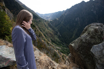 Naklejka premium a beautiful girl in a turquoise dress holds her hair and looks at the majestic beautiful mountains in summer. back view