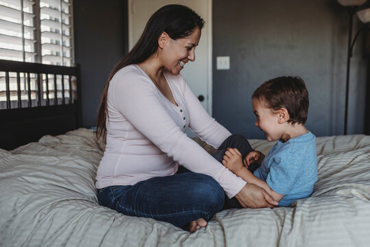 Laughing mid-30&rsquo;s mom tickling 5 yr old son on bed near window