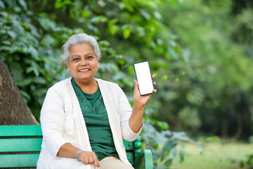 Indian senior woman showing smartphone screen at park.