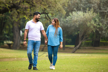 young indian couple holding hand each other and walking in park.
