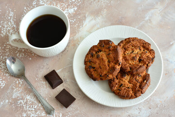 oatmeal cookies with chocolate chips on white plate with teaspoon and cup of coffee, close-up