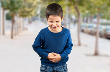 Young little boy kid wearing blue shirt walking down the street with his hand on his stomach...