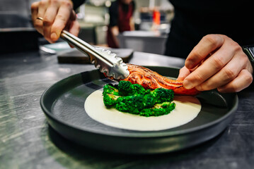 chef hand preparing a gourmet salmon steak with broccoli on restaurant kitchen