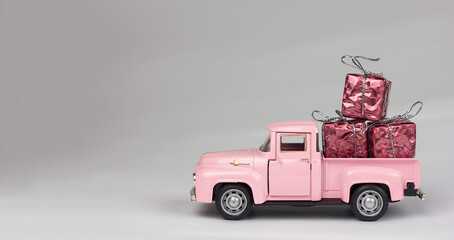  Car toy model pink pickup truck gift boxes on a gray background, delivery sale gifts, selective focus © Valentyna