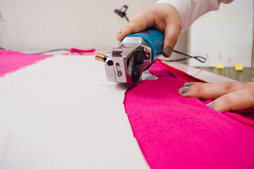 close up of mechanical fabric cutter cutting fuchsia fabric.