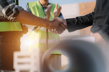 Obraz premium construction worker wearing a protective helmet and vest is holding his colleague's hand while working at the job site.
