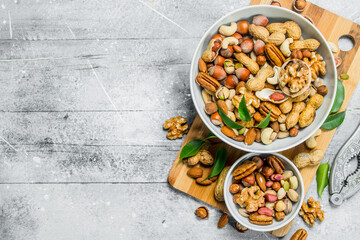 Different types of nuts in bowls with green leaves.