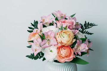 Beautiful bouquet of fresh colorful pastel ranunculus and lily flowers in full bloom with green fern leaves in vase against white background, close up. Spring bunch of blossoms.