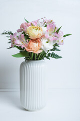 Beautiful bouquet of fresh colorful pastel ranunculus and lily flowers in full bloom with green fern leaves in vase against white background. Spring bunch of blossoms.