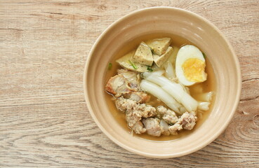 large rice noodles slice sausage with chop and crispy pork topping soft boiled egg in soup on bowl   