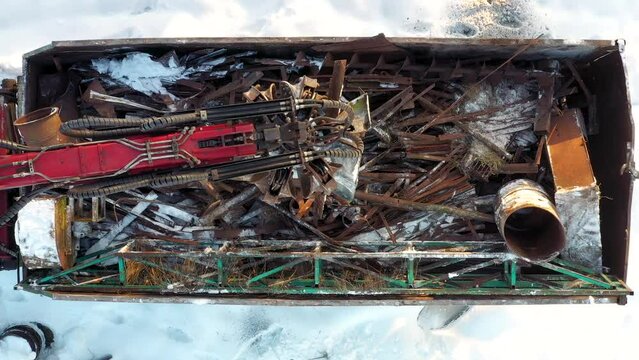 Excavator grabs scrap of rusty metal with bucket for secondary remelting and pours it into container of truck. Transportation to industrial enterprise for collection and processing of scrap metal.