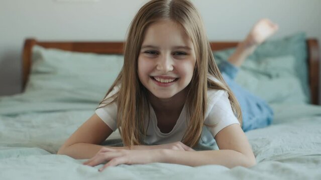 Pretty girl child lying in bed, looking at camera and smiling. Cute happy female kid in bedroom closeup portrait