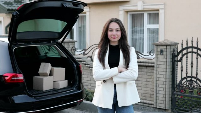 Young business woman standing at the car with parcels, coming home by car. The girl is standing and talking on mobile phone near the car. Concept of buying goods online and delivering them home