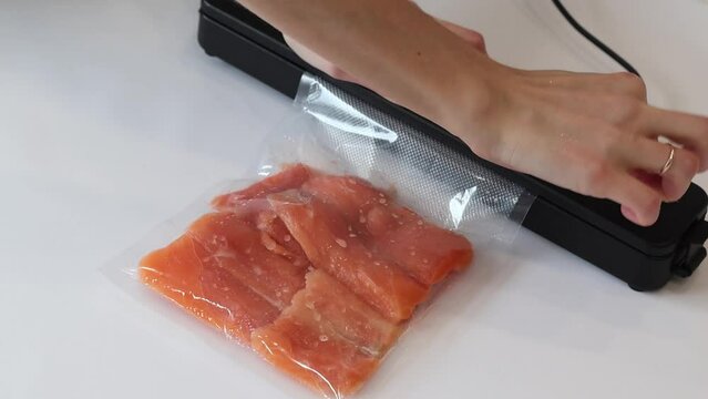Vacuum packaging machine packs salmon fillets in a vacuum bag for pickling or sous-vide cooking. Vacuuming process